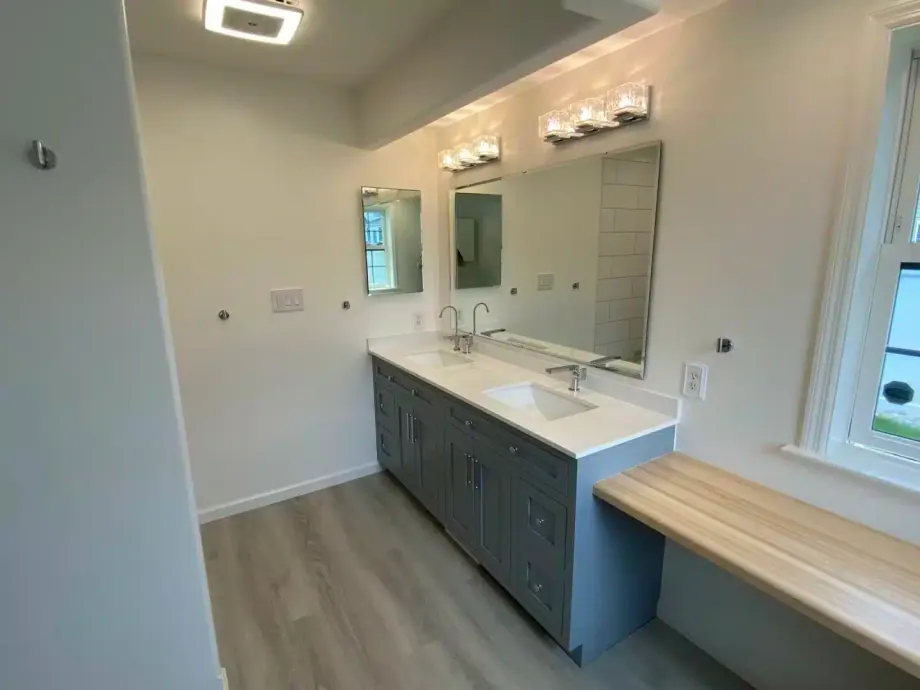 Remodeled bathroom with a blue double vanity, white countertop and a built-in wood bench