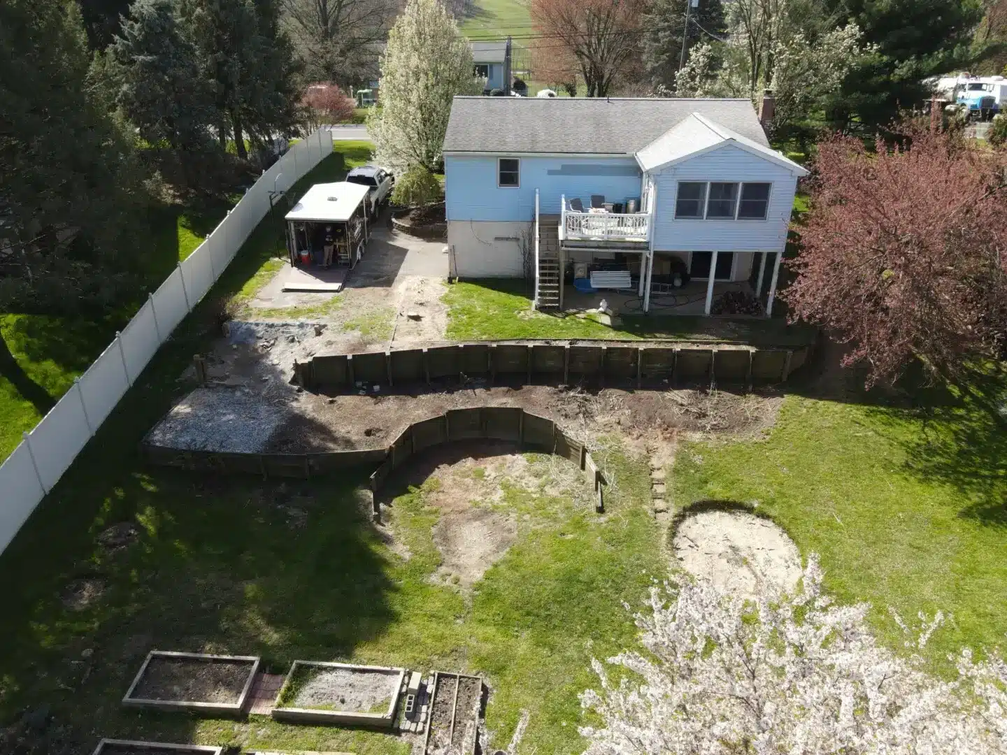 Aerial view of a residential backyard with an existing timber retaining wall, lawn, garden beds, and the rear of the home.